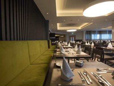 Modernes Restaurant mit grünen Sitzbänken, weißen Servietten und elegant gedeckten Tischen.