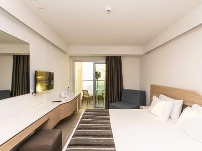 Modernes, helles Hotelzimmer mit Doppelbett, Schreibtisch, Wandspiegel und Balkon mit Vorhängen.