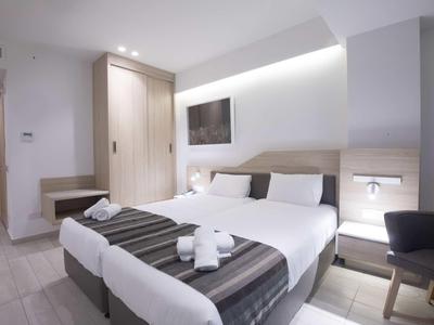 Helles Hotelzimmer mit zwei Einzelbetten, Holzschrank, Fernseher und modernem Dekor.