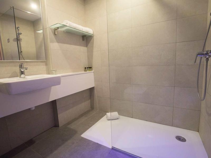 Modernes Badezimmer mit bodengleicher Dusche, großem Spiegel und schlichtem Waschbecken.