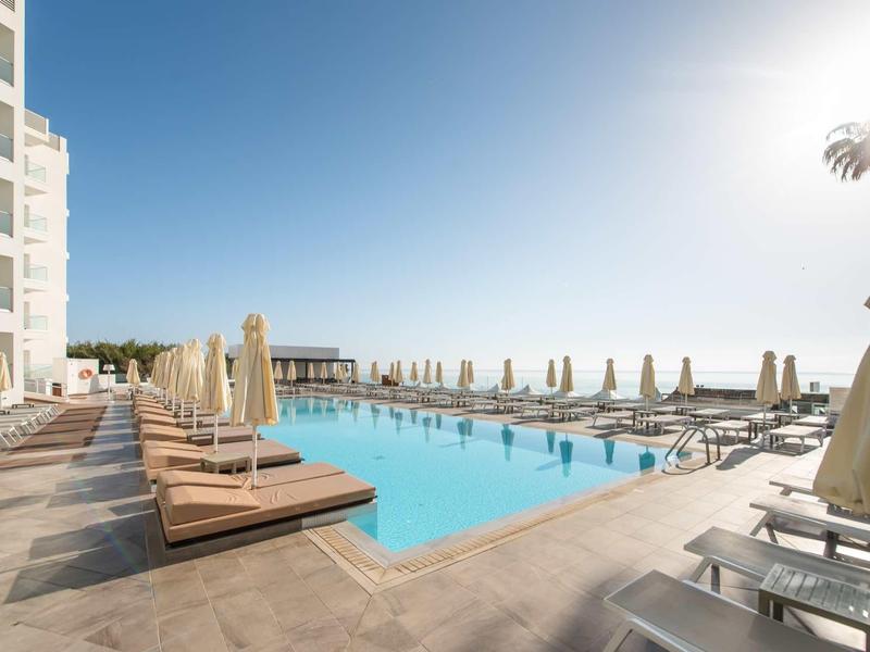 Moderner Hotelpool mit Liegen und Sonnenschirmen unter klarem blauem Himmel bei Sonnenlicht.