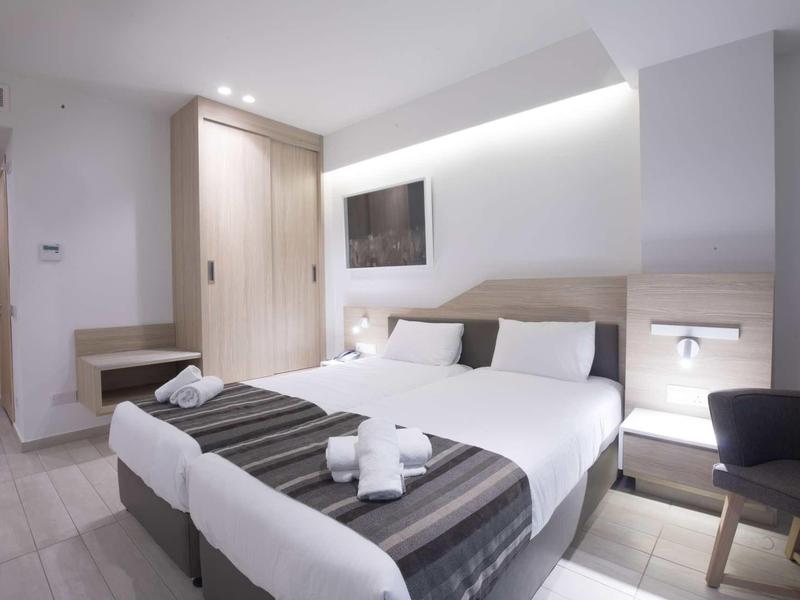 Modern eingerichtetes Hotelzimmer mit zwei Einzelbetten, hellen Holzmöbeln und schlichtem Design.