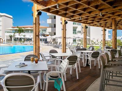 Terrazza esterna coperta con tavoli vuoti vista piscina sotto un cielo sereno.