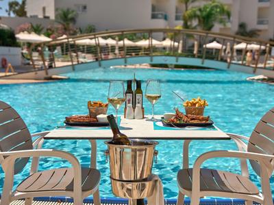 Ein gedeckter Tisch am Pool mit Snacks, Getränken und umgeben von Liegestühlen und Sonnenschirmen.