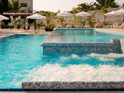 Moderner Hotelpool mit klarem Wasser, Whirlpools und Sonnenschirmen im Hintergrund.