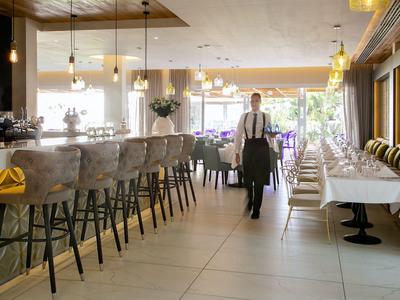 Heller Hotelrestaurantbereich mit Bar, Stühlen und einem Kellner im Gang.