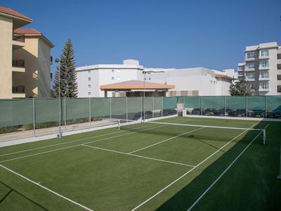 Ein Tennisplatz mit grünem Boden umgeben von Wohngebäuden bei blauem Himmel.