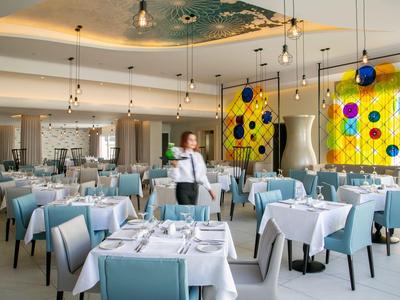 Modernes Restaurant mit blauen Stühlen, weißen Tischen und farbenfroher Wanddekoration.