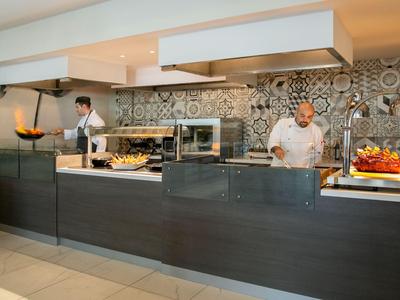 Hotelküche mit zwei Köchen, moderner Arbeitsfläche und dekorativer Fliesenwand.