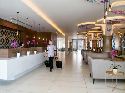 Luminosa hall dell'hotel con reception e un ospite che cammina con valigie.