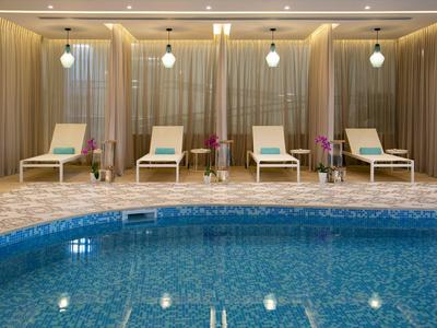 Innen-Pool mit blauem Wasser, umgeben von beigen Liegestühlen und warmen Wänden mit indirekter Beleuchtung.