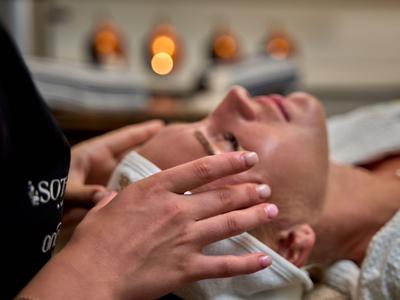 Frau erhält im Hotel eine entspannende Gesichtsmassage mit weichen Handbewegungen.