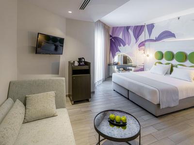 Modern eingerichtetes Hotelzimmer mit Doppelbett, Sofa und Flachbildfernseher.