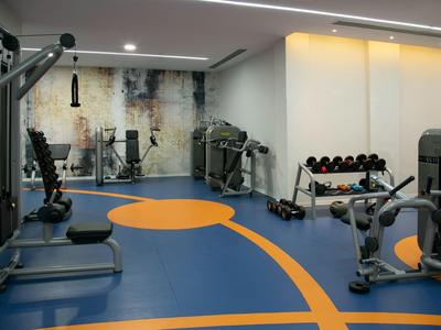 Ein moderner Fitnessraum mit verschiedenen Trainingsgeräten und einer blauen-orangefarbenen Bodenmarkierung.