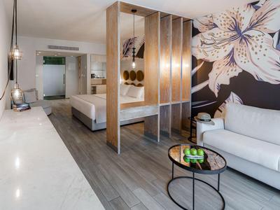 Modern eingerichtetes Hotelzimmer mit Bett, Sofa, Tisch und großer Blumenwand.