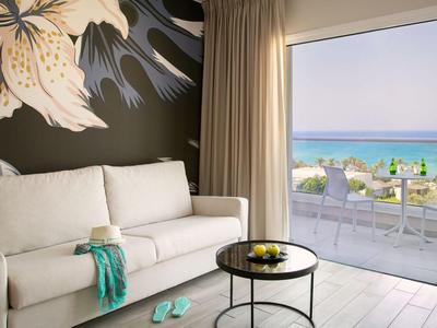 Modernes Hotelzimmer mit Sofa, Tisch und Balkon mit Meerblick und Stühlen.