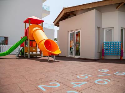 Kinderspielplatz mit Rutsche und Hüpffläche neben einem Gebäude in sonniger Umgebung.