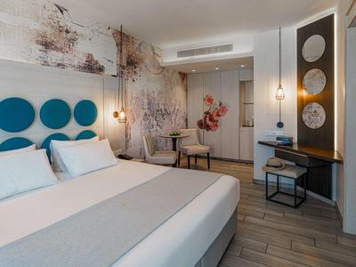 Modernes Hotelzimmer mit großem Bett, blauer Wanddeko, Schreibtisch und floraler Wandgestaltung.
