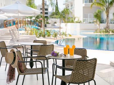 Diverse sedie e tavoli accanto a una piscina dell'hotel con bevande su un patio soleggiato.