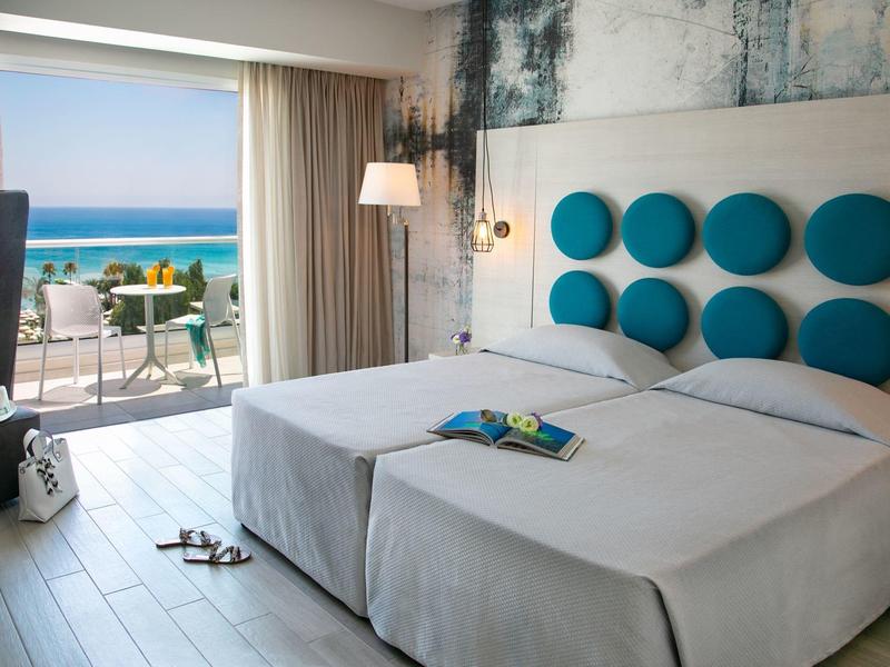 Helles Schlafzimmer mit zwei Betten, runden blauen Wanddekorationen und Blick auf das Meer.