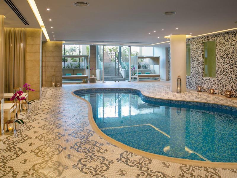 Elegantes Hallenbad mit organisch geformtem Becken, gemusterter Bodenfliese und großer Fensterfront.