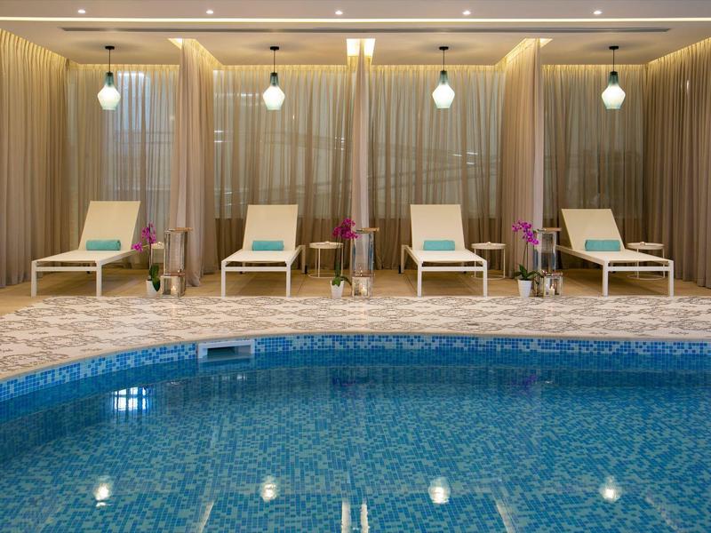 Innen-Pool mit blauem Wasser, umgeben von beigen Liegestühlen und warmen Wänden mit indirekter Beleuchtung.