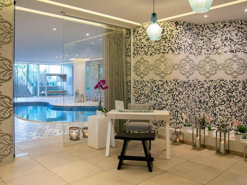 Moderner Raum mit gemusterten Wänden, weißem Tisch, schwarzem Hocker und Blick auf Innenpool.