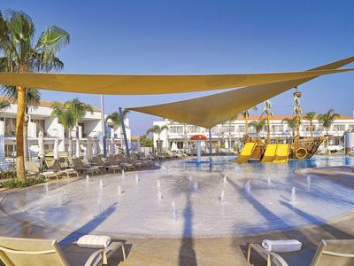 Kinder-Pool mit Wasserspielplatz, Sonnensegel und Liegestühlen in einem Hotelresort.
