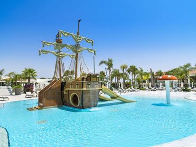 Ein Schwimmbad mit einem Piratenschiff-Spielplatz und Palmen im Hintergrund bei klarem Himmel.
