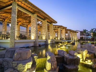 Beleuchtete Außenanlage eines Hotels mit Steinsäulen und Wasser in der Dämmerung.