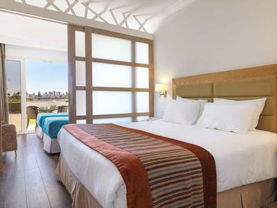 Helles Hotelzimmer mit zwei Betten, beiger Holzmöbel und großem Fenster mit Aussicht.