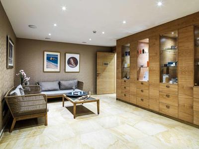 Moderner Wohnraum mit grauem Sofa, Holztisch, beleuchtetem Wandregal und hellem Fliesenboden.