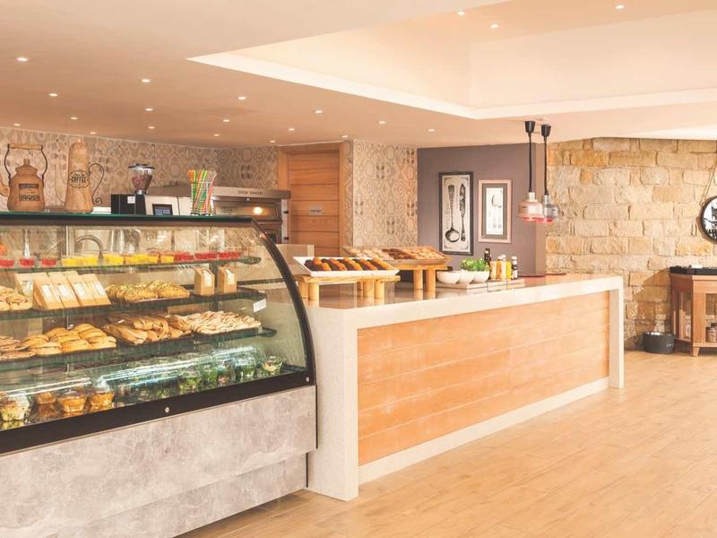Innenraum einer hellen Bäckerei mit Glasvitrine voller Backwaren und langem Verkaufstresen.
