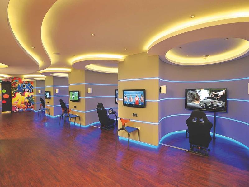 Moderne Gaming-Lounge mit geschwungenen Decken, LED-Beleuchtung und mehreren Spielstationen.