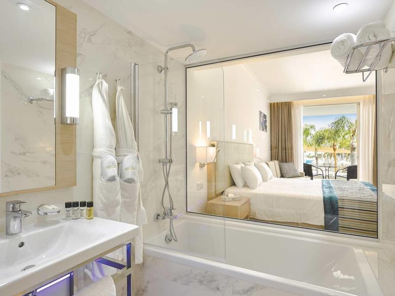Modernes Badezimmer mit Badewanne, Regendusche und Blick ins helle, gemütliche Schlafzimmer.
