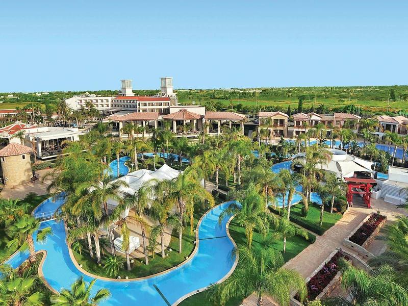 Große Resortanlage mit Pool, Palmen und Gebäuden vor klarem blauem Himmel.