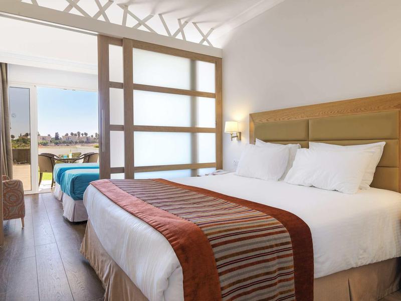 Helles Hotelzimmer mit zwei Betten, beiger Holzmöbel und großem Fenster mit Aussicht.