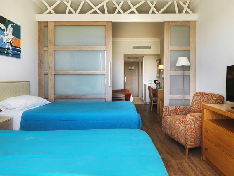 Zimmer mit zwei blauen Einzelbetten, einem gemusterten Sessel und einem Holzschrank.