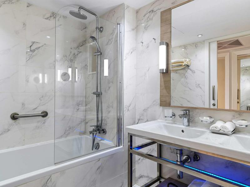 Moderne Badezimmer mit weißem Marmor, großer Badewanne, Glasdusche und beleuchtetem Spiegel.