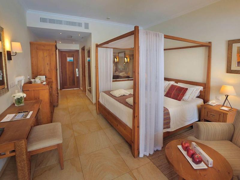 Gemütliches Hotelzimmer mit Himmelbett, Sessel, Holzmöbeln und warmem Farbton.