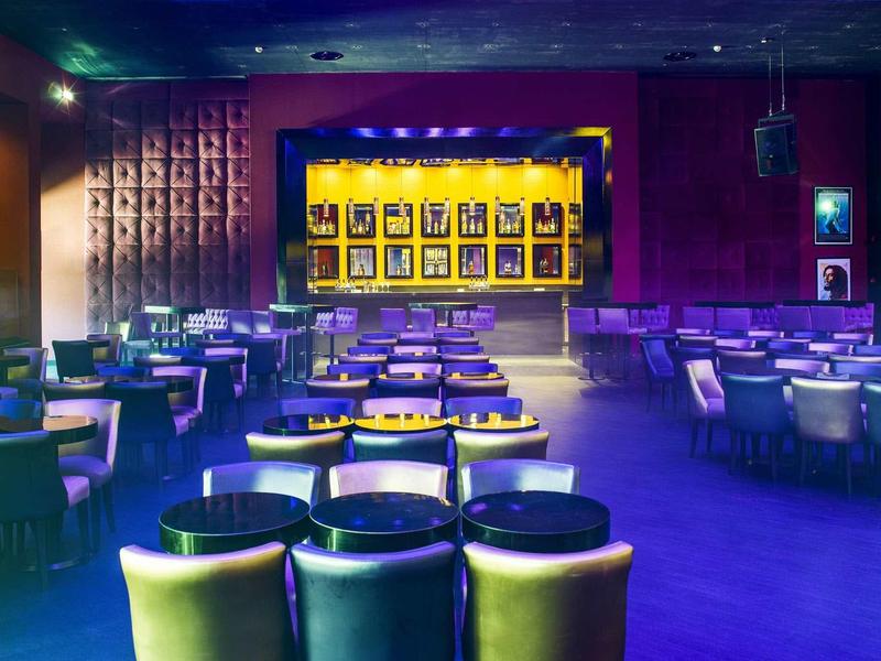 Innenraum eines Theaters mit Stuhlreihen und einer Bühne mit gelbem Hintergrund und Bildern.