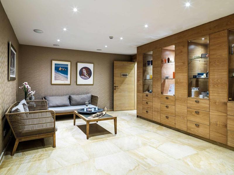 Moderner Wohnraum mit grauem Sofa, Holztisch, beleuchtetem Wandregal und hellem Fliesenboden.