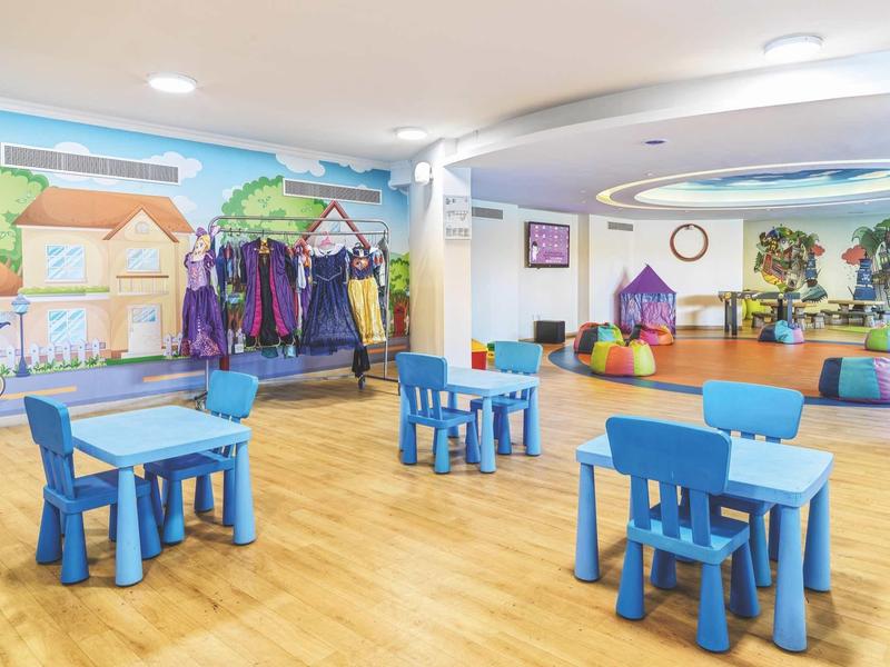 Bunte Kinderecke mit blauen Tischen und Stühlen, Holzfußboden und bunter Wandgestaltung.