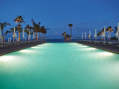 Oświetlony basen z leżakami i palmami o zmierzchu