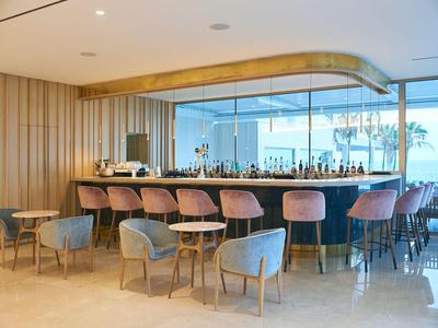 Nowoczesny bar hotelowy z hokerami i stolikami, duże okna z widokiem na miasto.