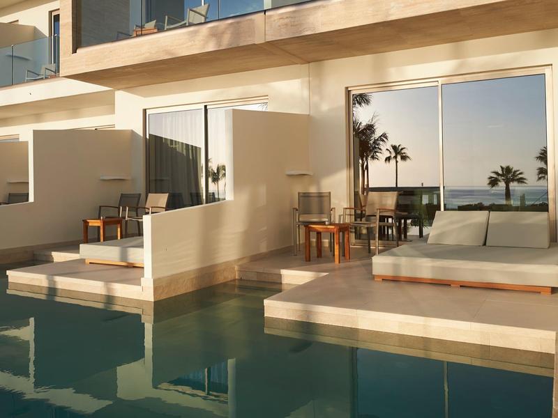 Modern hotel pool area with terrace and sea view at sunset.