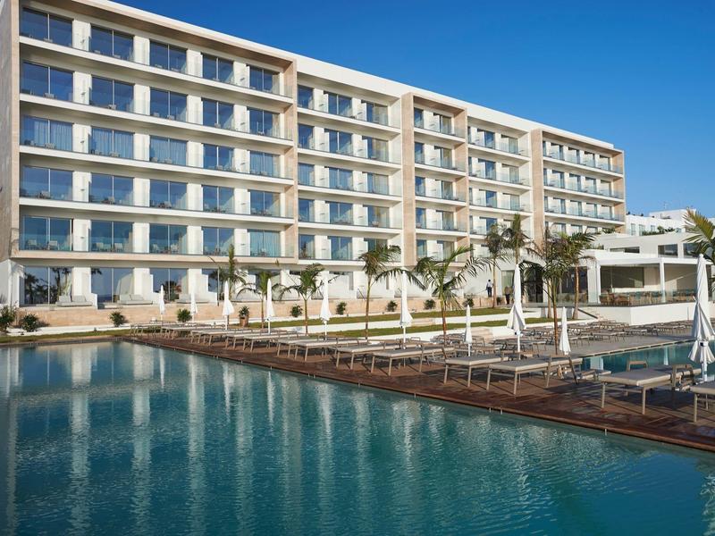 Modern hotel with large windows and outdoor pool under clear sky.