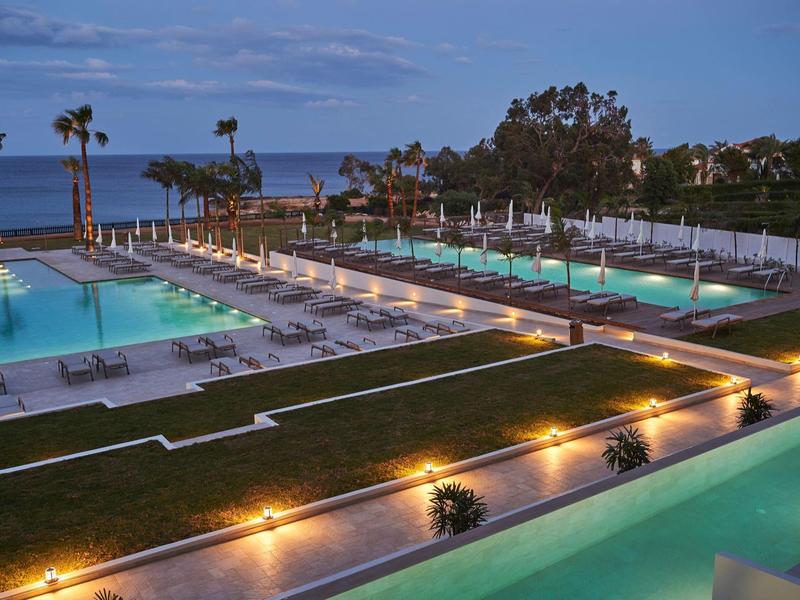 Evening view of a modern hotel pool with palm-lined beach in the background