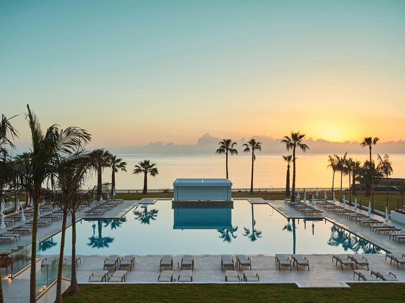 Large hotel pool with lounge chairs and palm trees at sunrise.