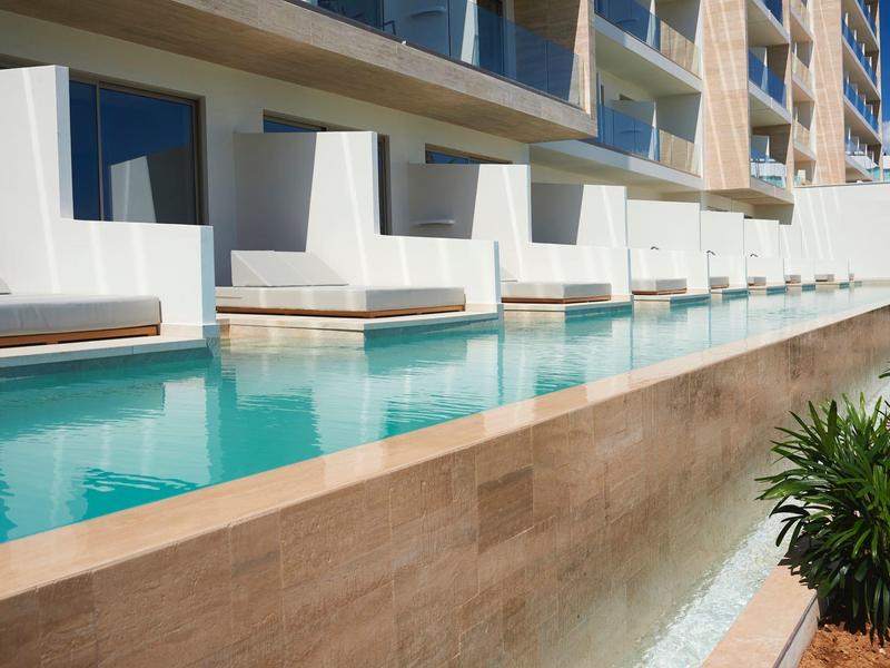 Modern pool area beside a hotel with white loungers and clear blue water.